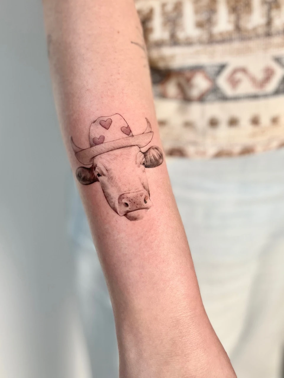 cow in a hat fine line tattoo on forearm